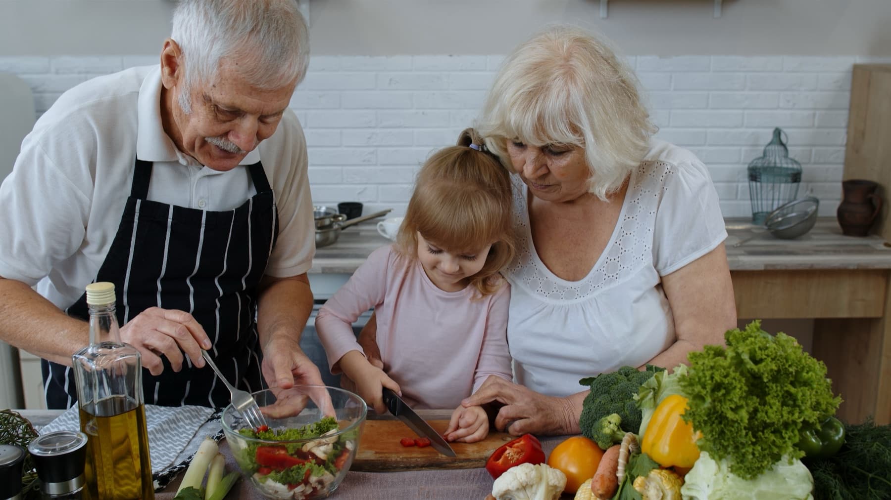 Grandparents and their granddaughter making a fresh salad together in the kitchen